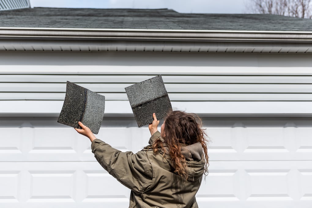 woman inspecting shingles before asking insurance roof replacement questions