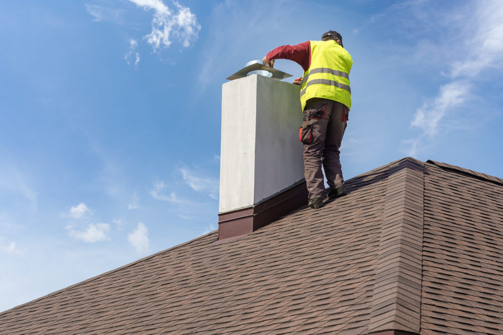 roof repair tips man in yellow safety vest repairing chimney on asphalt roof