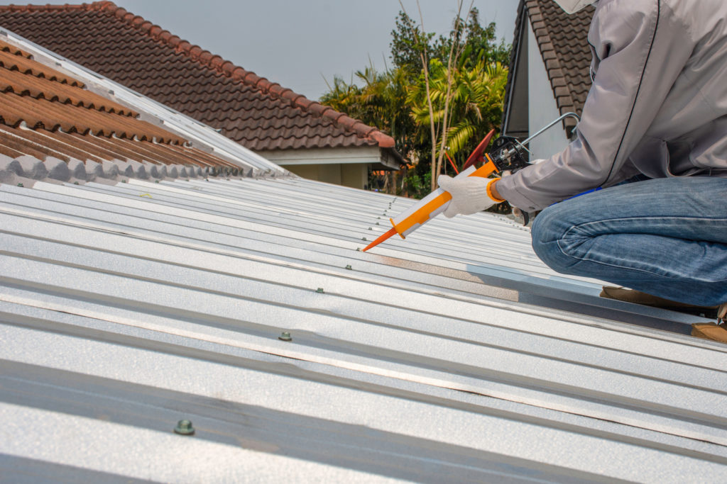 roof repair tips worker caulking metal roof panel